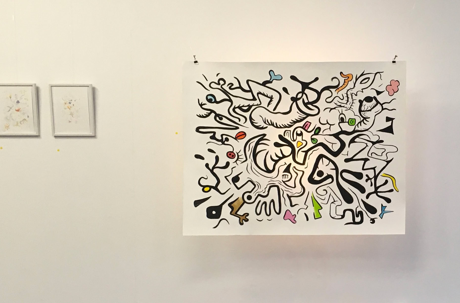 Deux petites œuvres encadrées à gauche et une grande œuvre abstraite colorée à droite accrochées sur un mur blanc.