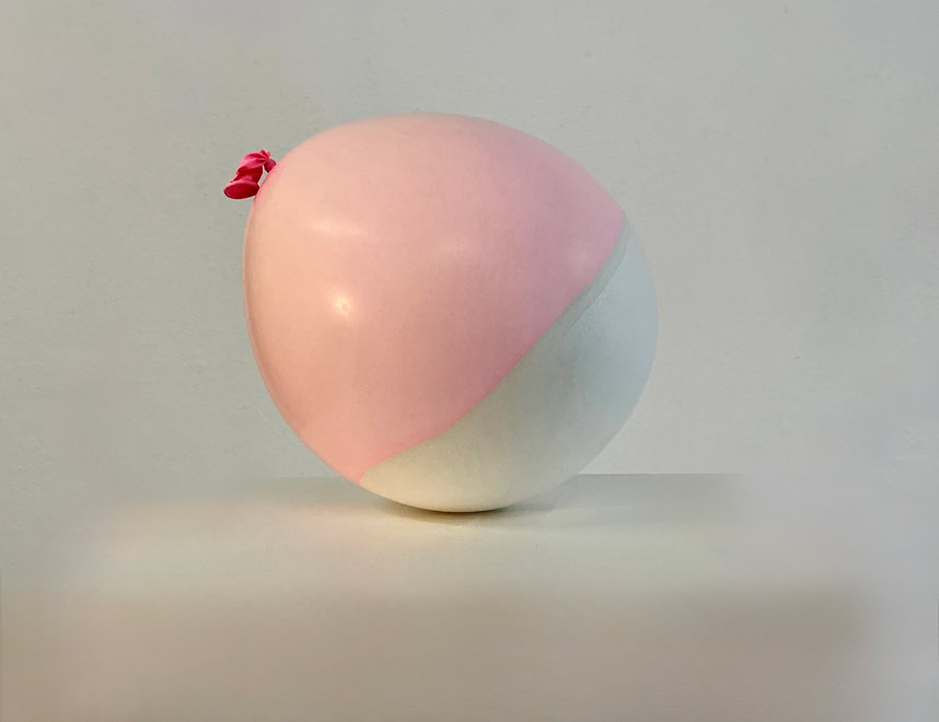 Coquille en plâte et latex d'un ballon bicolore rose et blanc sur une surface blanche.