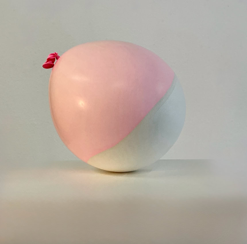 Coquille en plâte et latex d'un ballon bicolore rose et blanc sur une surface blanche.