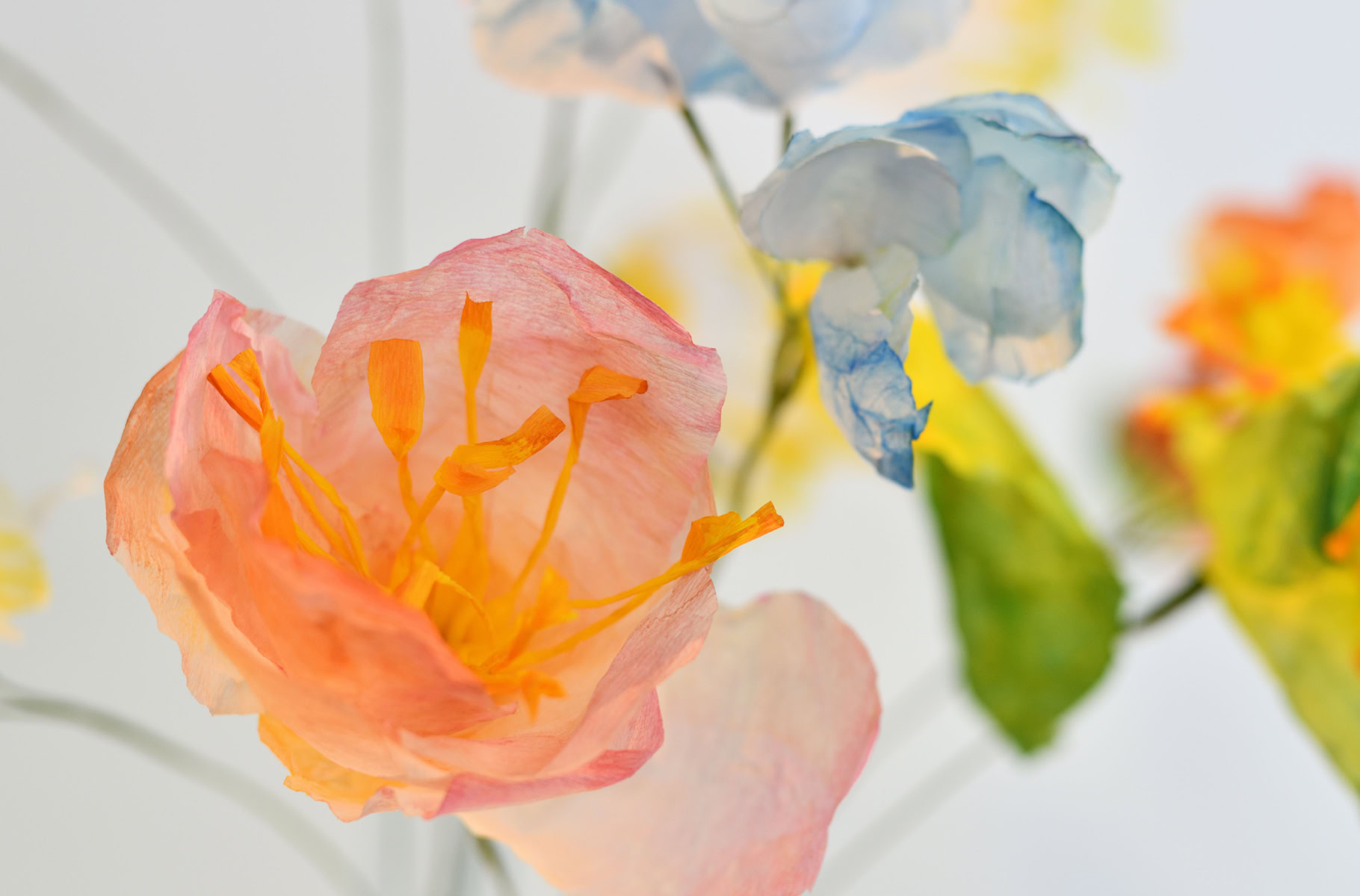 Fleurs en papier aux couleurs pastel, avec des pétales roses et jaunes, et des feuilles vertes.