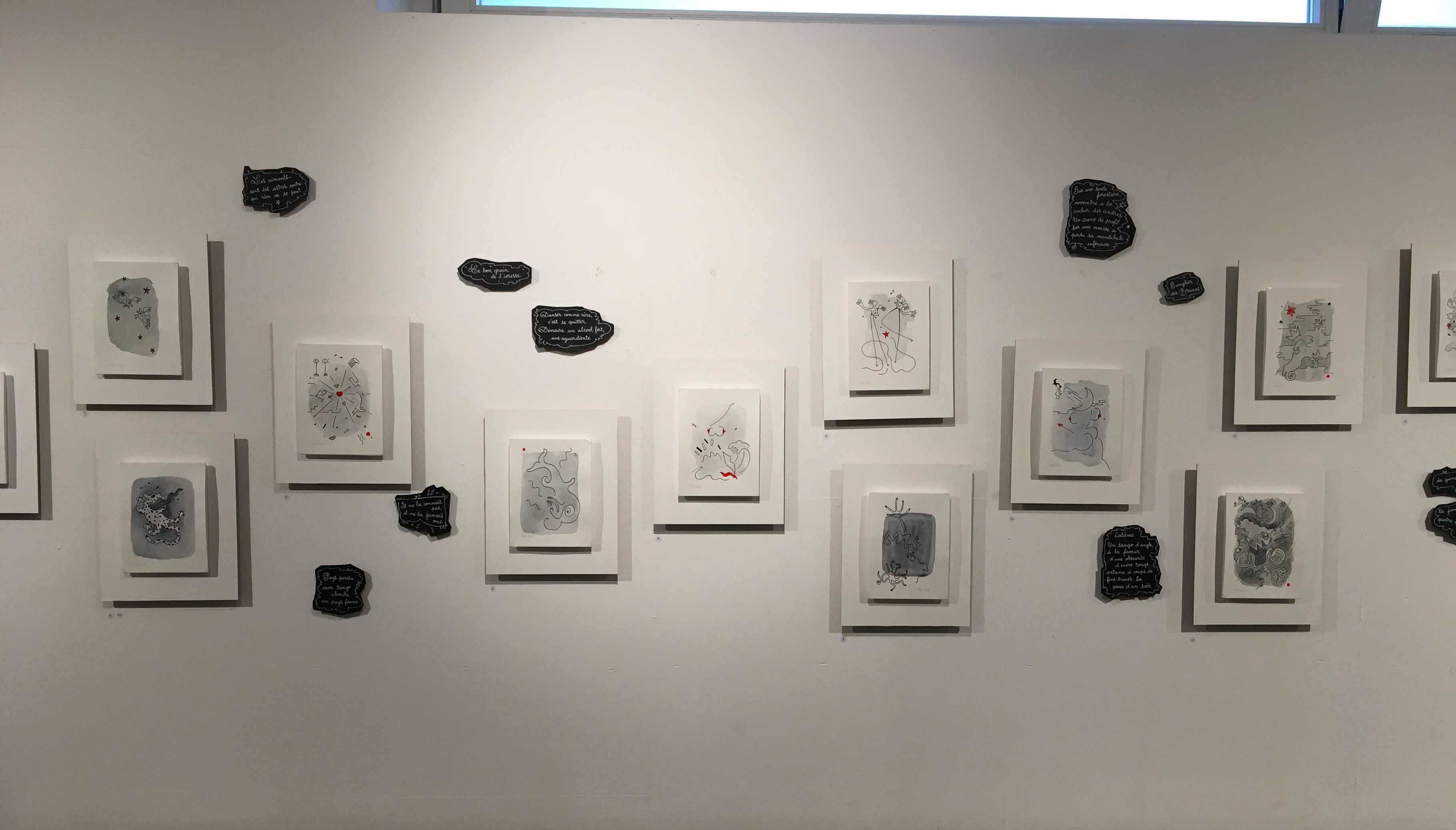 Mur blanc avec plusieurs cadres alignés contenant des dessins en noir et blanc, entourés de petites formes noires.