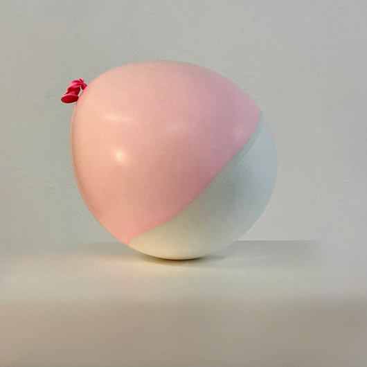 Coquille en plâte et latex d'un ballon bicolore rose et blanc sur une surface blanche.