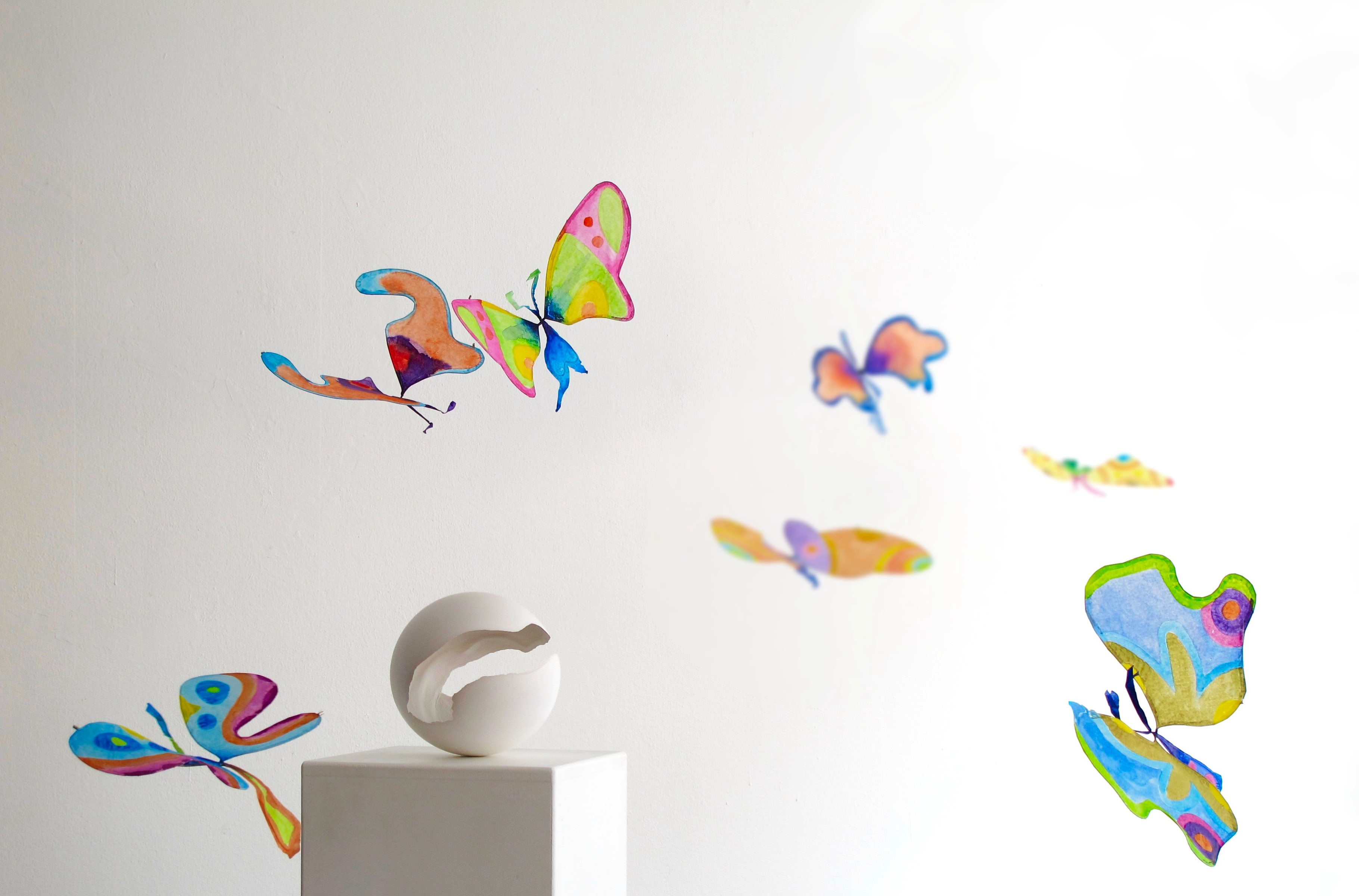 Sculpture en forme de coquille blanche sur un socle, entourée de papillons colorés sur un fond blanc.