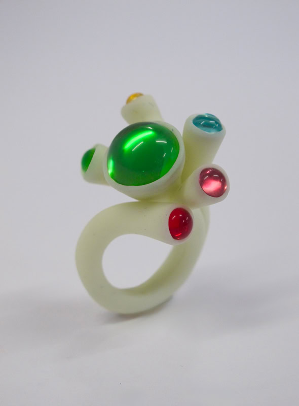 Bague en résine blanc avec des pierres colorées vertes, rouges et bleues.