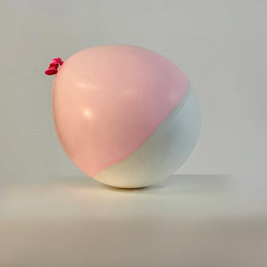 Coquille en plâte et latex d'un ballon bicolore rose et blanc sur une surface blanche.