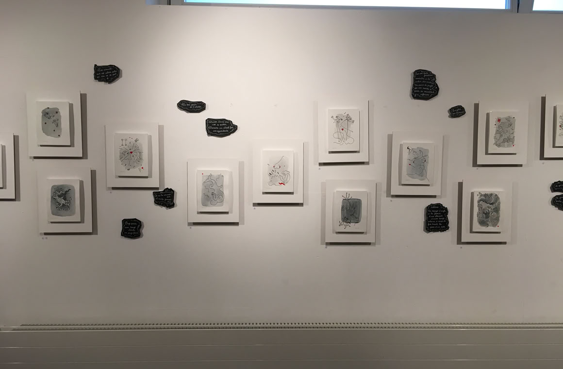 Mur blanc avec plusieurs cadres alignés contenant des dessins en noir et blanc, entourés de petites formes noires.